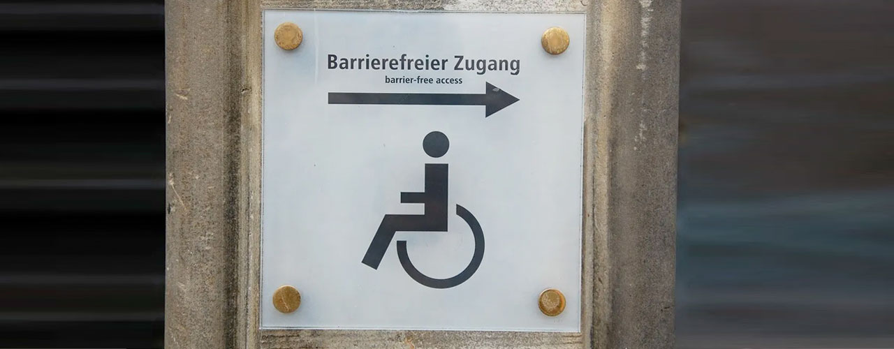 Wegweiser mit vier goldenen Befestigungspunkten Barrierefreier Zugang mit Pfeil und Rollstuhl als Piktogramm und englischer Beschriftung barrier-free access