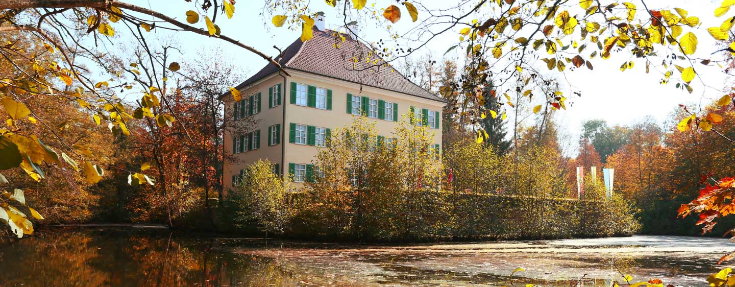 Sisi Schloss in Unterwittelsbach im Herbst mit gefärbtem Laub an den Bäumen und Sträuchern und farbigen Fahnen am Schloss