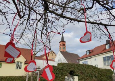 Herzen aus Papier der Valentinsüberraschung an einem Ast eines Baumes in Friedberg. Im Hintergrund die Friedberger Altstadt sowie eine Kirche.