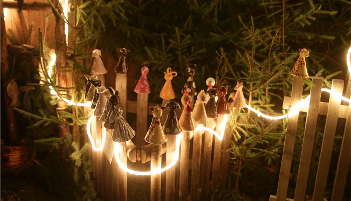 Weihnachtliche Ton-Männchen stecken auf einem Holzzaun mit Beleuchtung