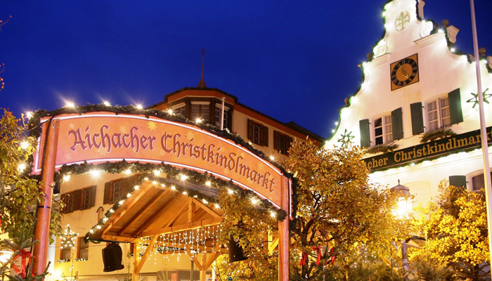 Eingangsportal des Aichacher Christkindlmarktes mit beleuchtetem Rathaus im Hintergrund