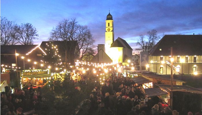 Weihnachtsmarkt im Schloss Affing mit vielen Besuchern und Beleuchtung, im Hintergrund der beleuchtete Kirchturm