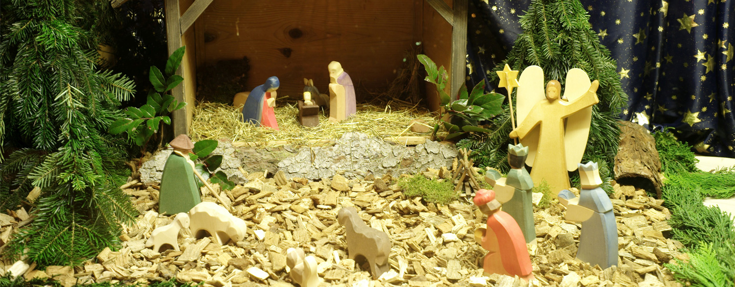 Krippe aus Holzfiguren mit Jesus, Maria und Josef, Hirten mit Schafen, Heilige Drei Könige und einem Engel auf Heu, Holzspäne und Tannenreisig