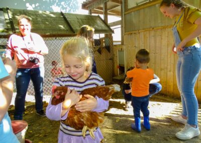 Kinder und Erwachsene stehen in einem Hühnerstall und tragen ein Huhn auf dem Arm