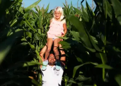 Vater hebt Tochter auf seine Schultern. Sie befinden sich in einem Maislabyrinth.