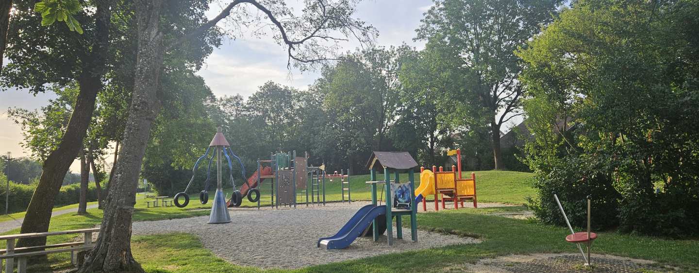 Spielplatz Aichach Foto: ©Landratsamt Verschiedene Rutschen, ein Karussell und ein Klettergerüst stehen auf dem hier abgebildeten Spielplatz mit Kiesboden.